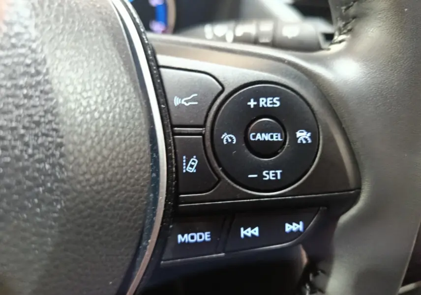 Gros plan sur les commandes au volant côté droit du Toyota RAV4 hybride, avec boutons de régulateur et mode audio.