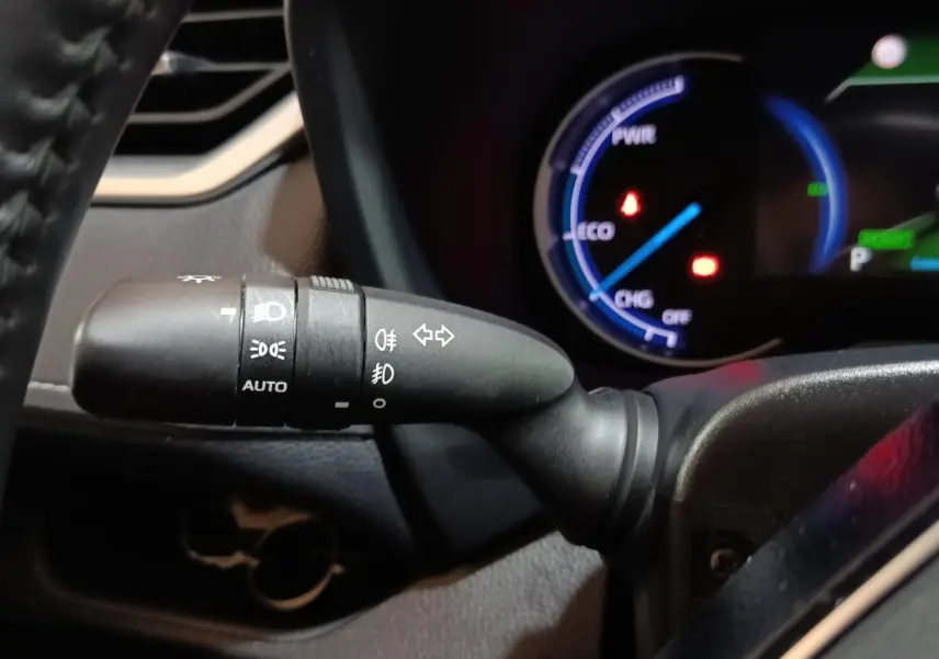 Gros plan sur la commande des phares et clignotants du Toyota RAV4 Hybride 2WD, avec tableau de bord numérique en arrière-plan.