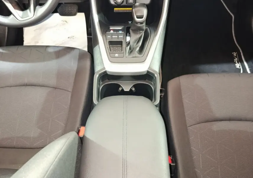 Vue intérieure centrée sur la console centrale noire du Toyota RAV4 hybride avec sièges tissu foncé et volant partiel.