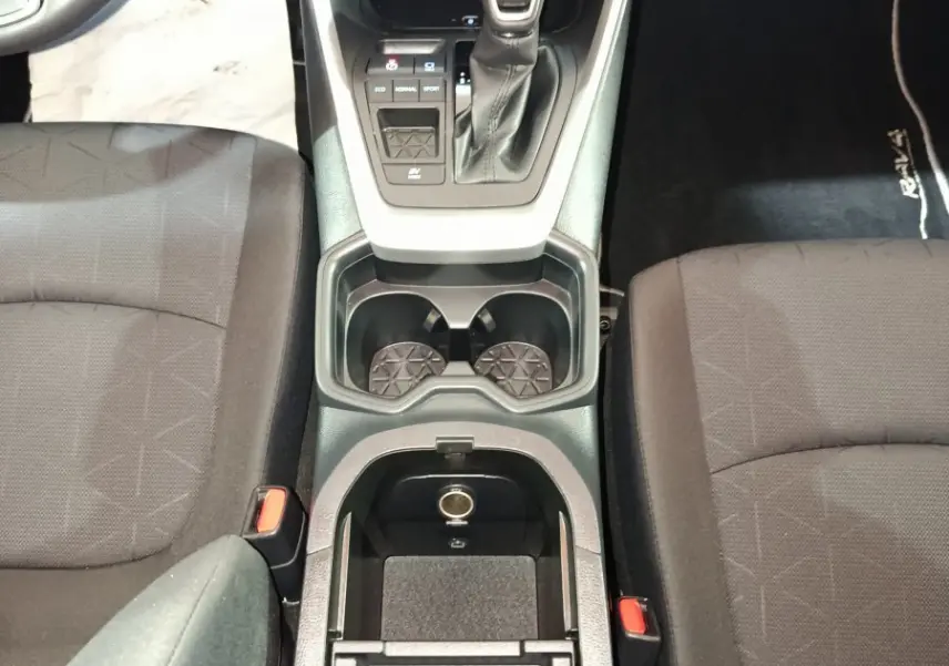 Vue plongeante sur la console centrale noire du Toyota RAV4 hybride avec levier de vitesse et sièges tissu gris.