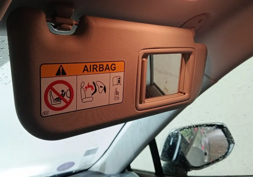 Vue intérieure du pare-soleil côté conducteur beige avec miroir et avertissement airbag, rétroviseur extérieur visible.
