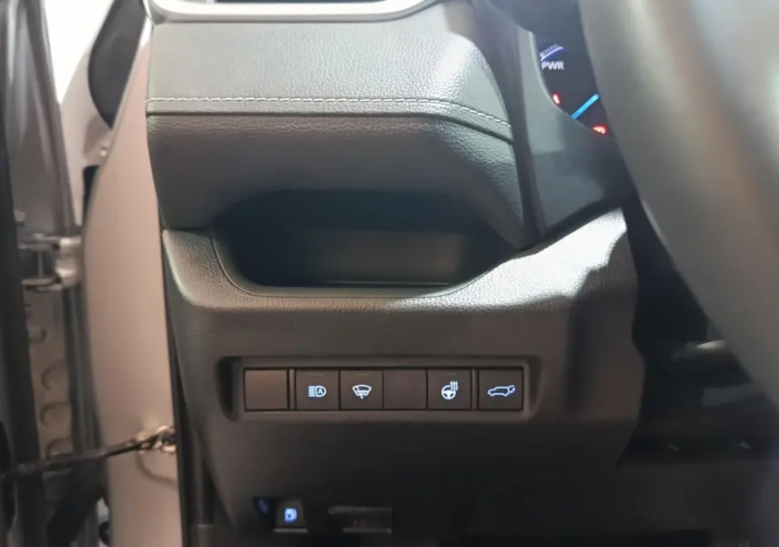 Vue rapprochée du tableau de bord côté gauche du Toyota RAV4 hybride 2021, boutons de commandes éclairés sur plastique noir.