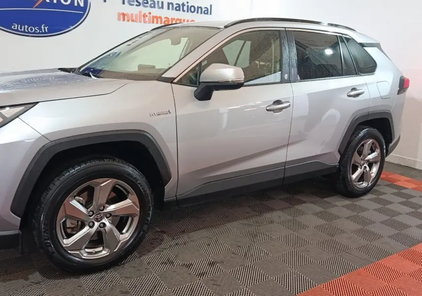 Vue de profil côté gauche d'un Toyota RAV4 hybride gris clair avec jantes alliage et badges Hybrid visibles.