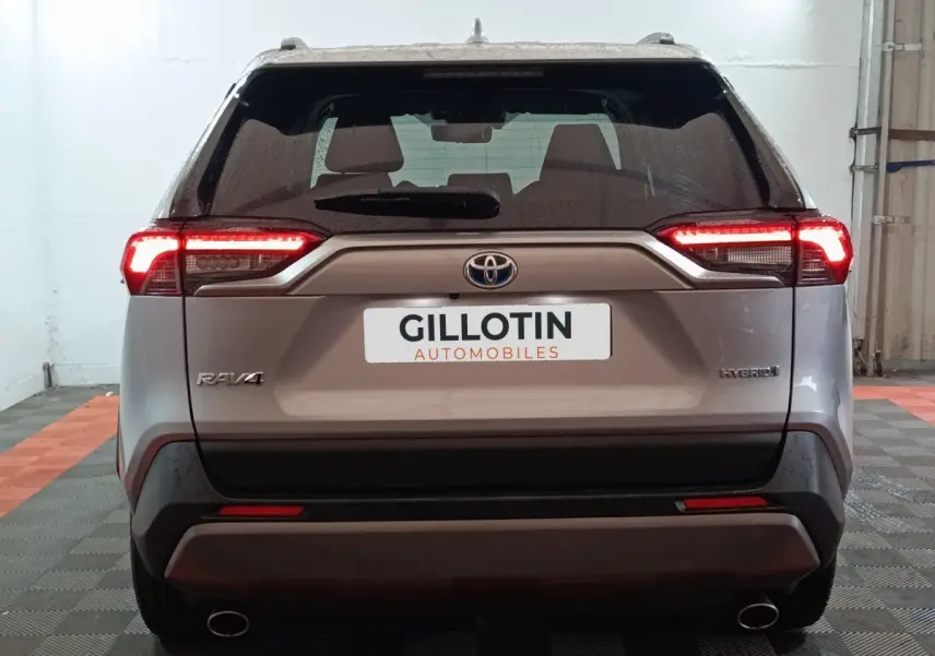 Vue arrière du Toyota RAV4 hybride gris avec feux LED allumés dans un garage fermé.