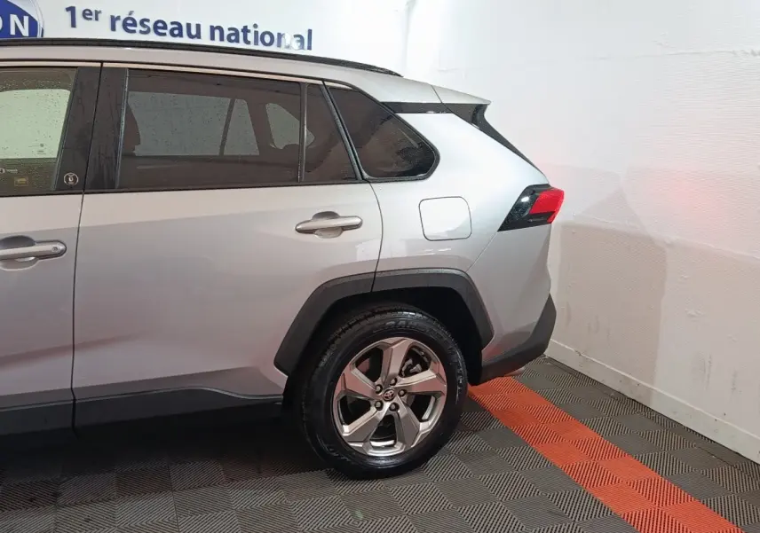 Vue latérale droite arrière d'un Toyota RAV4 hybride gris clair avec jantes alliage et feux arrière LED.
