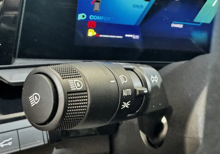 Gros plan sur la commande des phares automatique du Renault Espace noir 2025, avec écran multifonctions en arrière-plan.