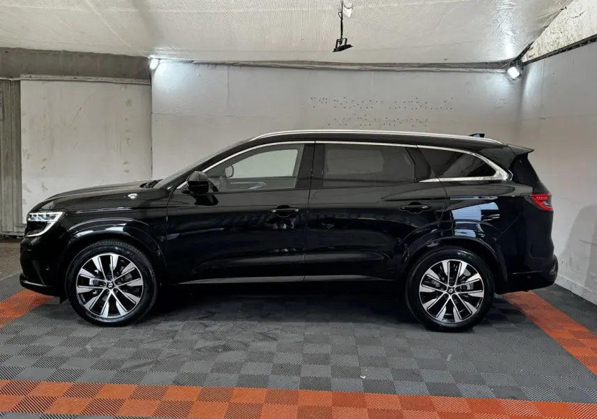Profil côté gauche d’un Renault Espace noir 2025 avec rails de toit chromés dans un garage.