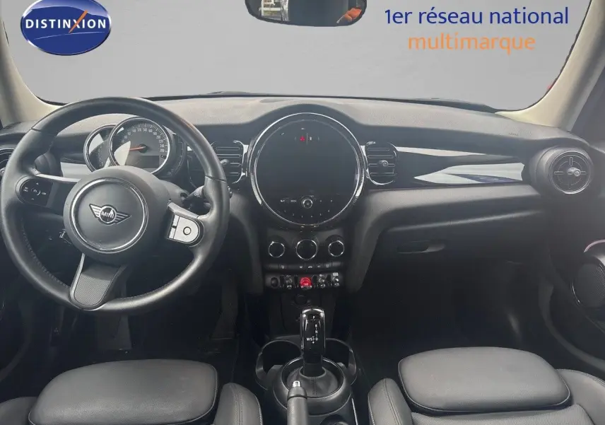 Intérieur avant d'une MINI 1.5 136CH gris, tableau de bord noir avec volant et console centrale visibles.