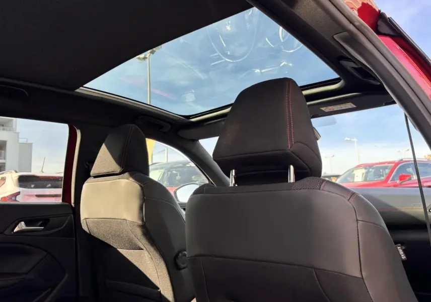 Vue intérieure arrière des sièges avant noirs avec surpiqûres rouges et toit panoramique en verre d'une Peugeot 308 rouge foncé GT Line.