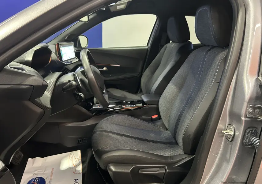 Vue intérieure côté conducteur du Peugeot 2008 gris 2025 avec sièges tissu et tableau de bord moderne équipé d'un écran tactile.
