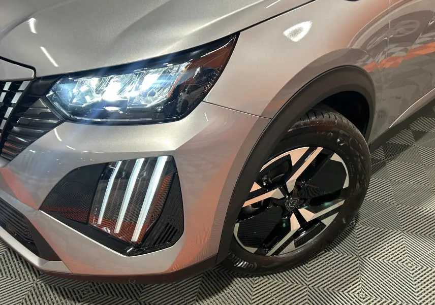 Gros plan sur l'avant droit gris métallisé du Peugeot 2008 Allure Hybrid 145 avec phares LED et jante alliage noire.