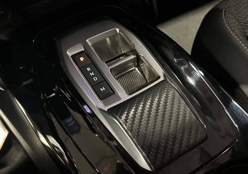 Gros plan sur la console centrale noire brillante du Peugeot 2008 Allure Hybrid 145 avec levier de vitesses automatique et insert carbone.