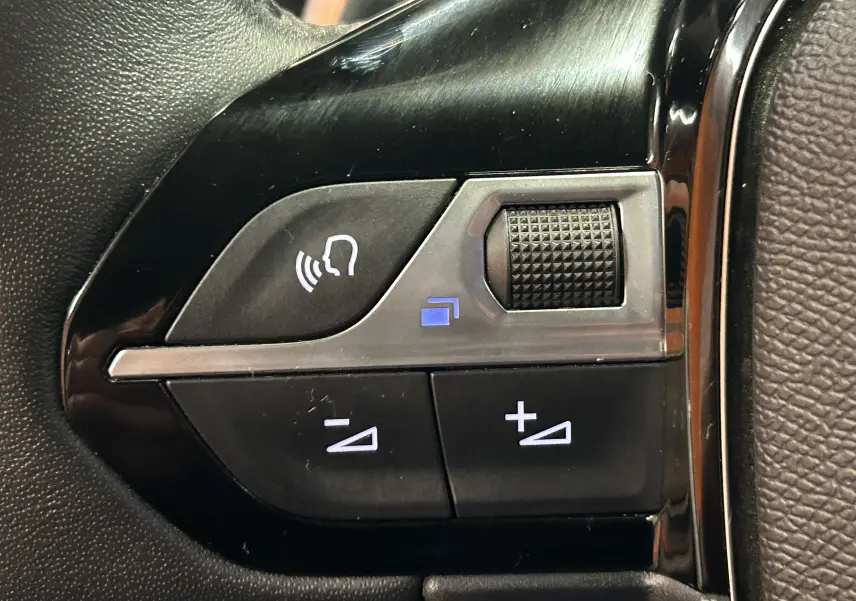 Gros plan sur les commandes du volant noir du Peugeot 2008 Allure Hybrid 145 gris, avec boutons de volume et reconnaissance vocale.