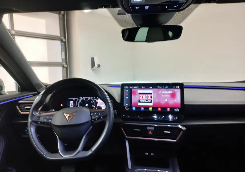 Vue intérieure du tableau de bord du CUPRA Formentor 2023, avec éclairage d'ambiance bleu et écran tactile central allumé.