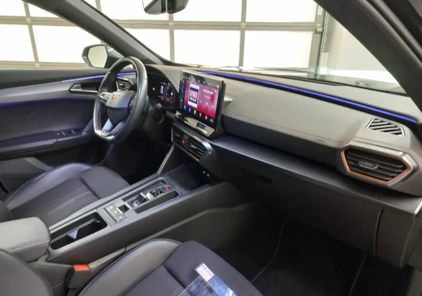 Vue intérieure côté conducteur du CUPRA Formentor 2023 avec éclairage d'ambiance bleu et tableau de bord moderne noir et beige.