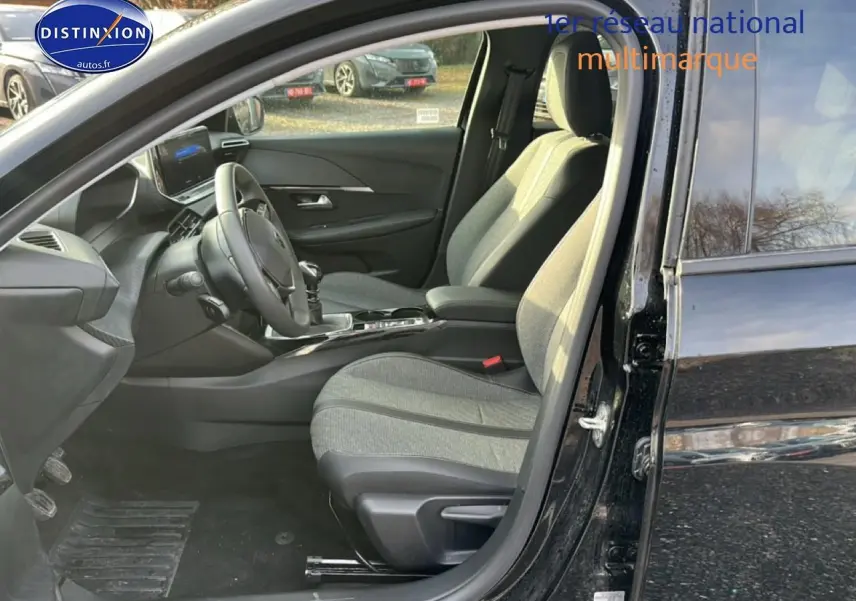 Intérieur de la Peugeot 208 1.2 PureTech 100 Allure 2024 noir, vue côté conducteur avec sièges tissu gris et volant multifonction.