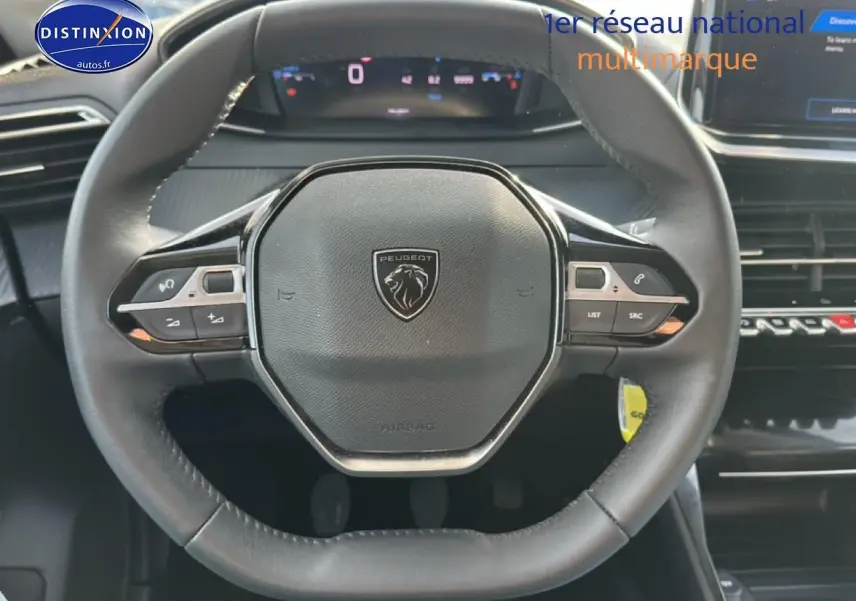 Vue rapprochée du volant noir de la Peugeot 208 1.2 PureTech 100 Allure 2024 avec commandes intégrées et tableau de bord numérique.