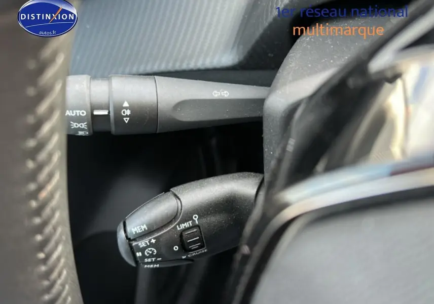 Gros plan sur les commandes au volant côté gauche d’une Peugeot 208 noire 2024, avec régulateur de vitesse et clignotants.