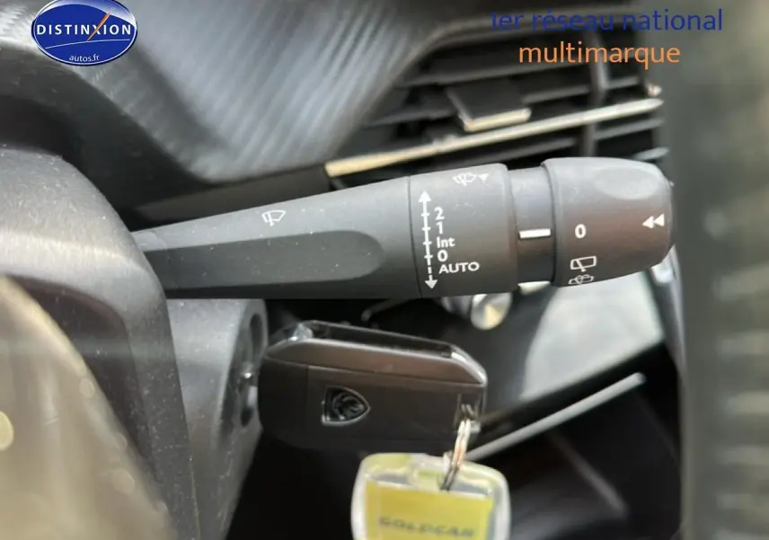 Gros plan sur la commande d'essuie-glace et la clé insérée dans le contact d'une Peugeot 208 noire, intérieur visible.