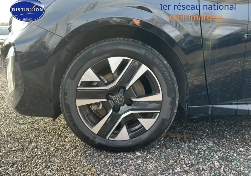 Gros plan sur la roue avant gauche avec jante alu bicolore du Peugeot 208 noir 1.2 PureTech 100 Allure 2024.