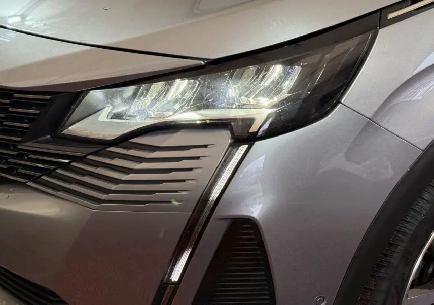 Gros plan sur le phare avant droit et la calandre d’un Peugeot 5008 gris clair avec éclairage LED distinctif.