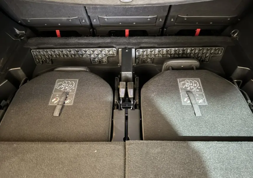 Vue plongeante sur le coffre du Peugeot 5008 gris clair avec sièges arrière rabattus et sangles de déploiement visibles.