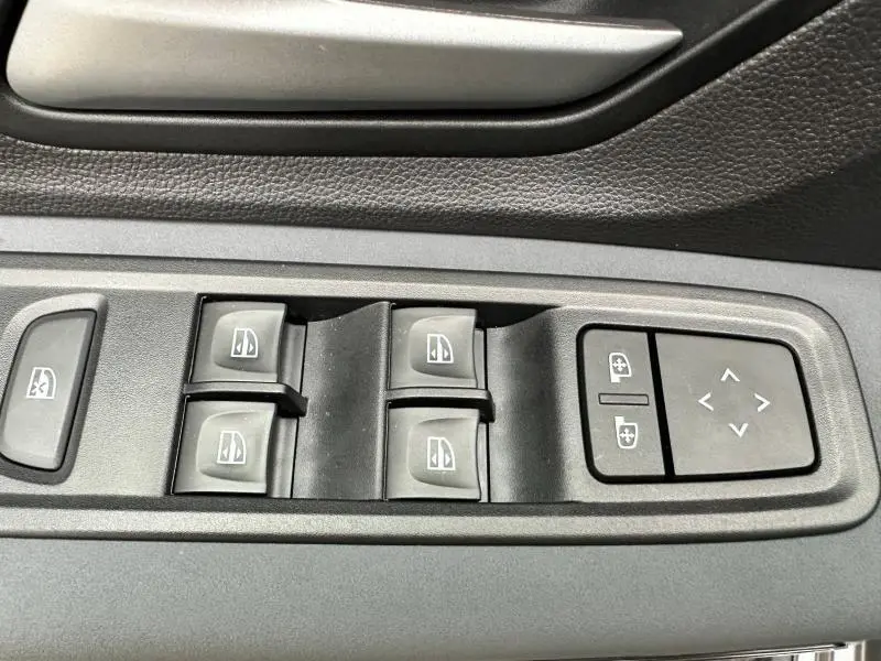 Gros plan sur les commandes des vitres électriques et des rétroviseurs côté conducteur du Dacia Jogger gris Schiste métallisé.
