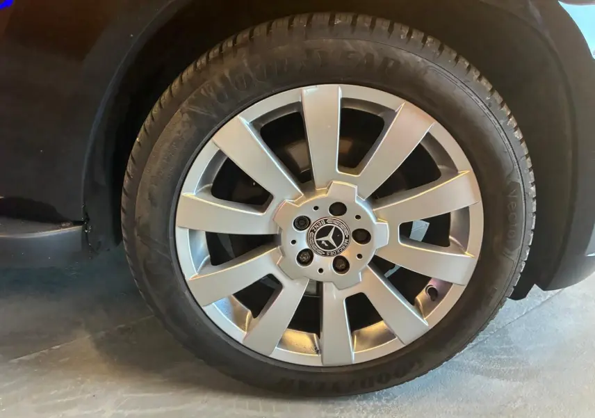 Gros plan sur la roue avant droite d’un Mercedes GLK noir, jante alliage argentée avec logo Mercedes central.