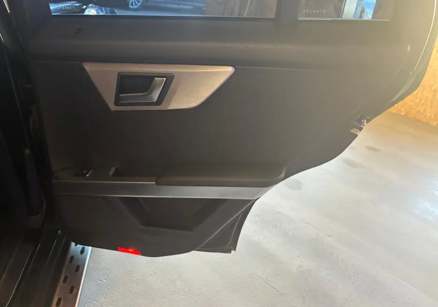 Vue intérieure de la porte arrière gauche noire d'un Mercedes GLK 220 CDI avec poignée argentée et éclairage rouge au bas.