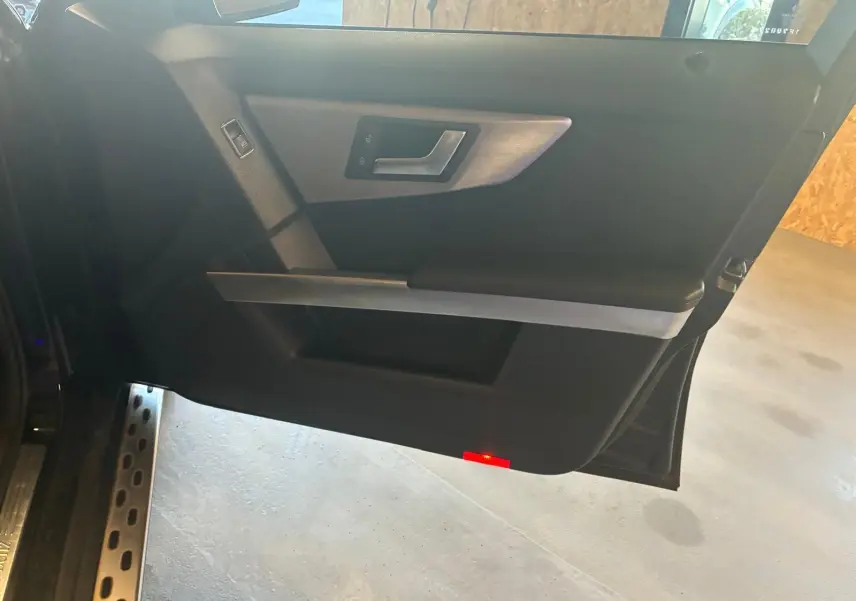 Vue intérieure de la porte côté gauche noire d’un Mercedes GLK 220 CDI avec poignée argentée et éclairage rouge en bas.