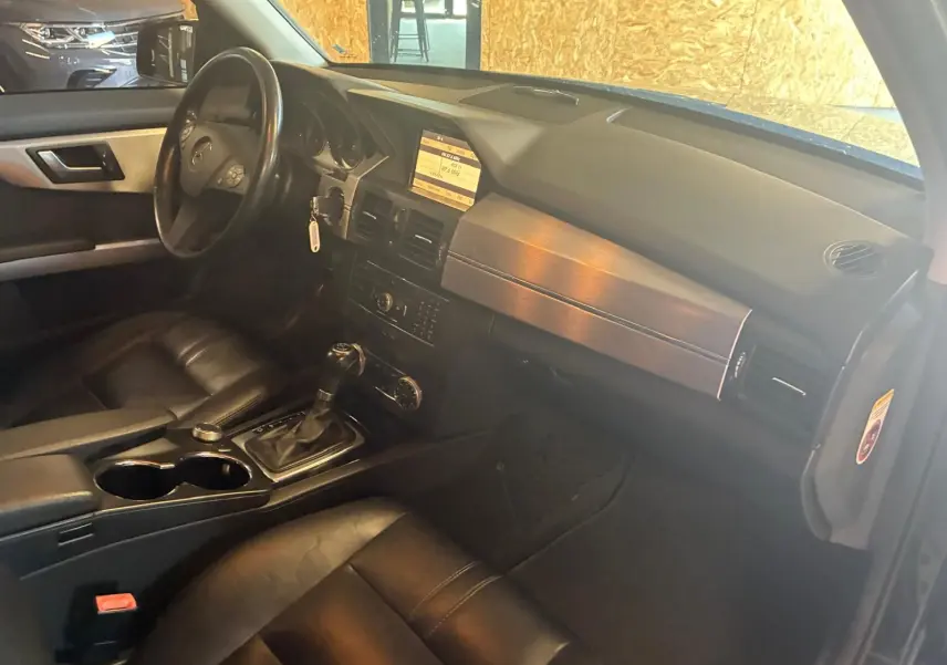Vue intérieure côté conducteur du Mercedes GLK 220 CDI noir de 2012, avec tableau de bord, volant et console centrale en cuir noir.
