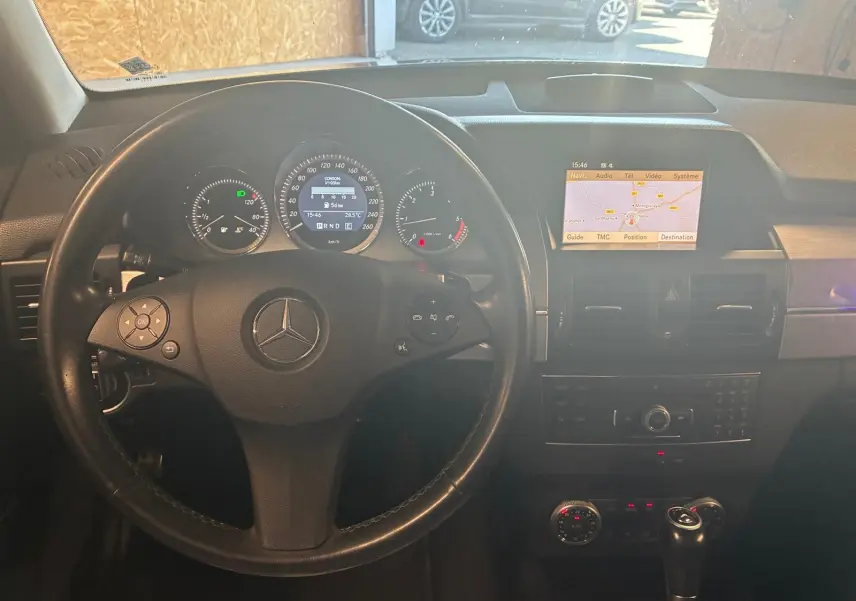 Vue intérieure du tableau de bord noir d'un Mercedes GLK 220 CDI 2012, avec volant cuir et écran GPS allumé.