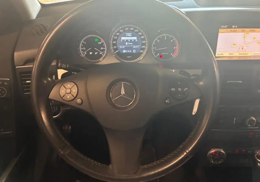 Vue rapprochée du volant noir de Mercedes GLK 220 CDI 2012 avec tableau de bord et écran GPS allumé.