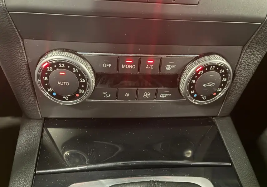 Gros plan sur la console centrale noire du Mercedes GLK 2012, montrant les commandes de climatisation automatique avec affichage digital.