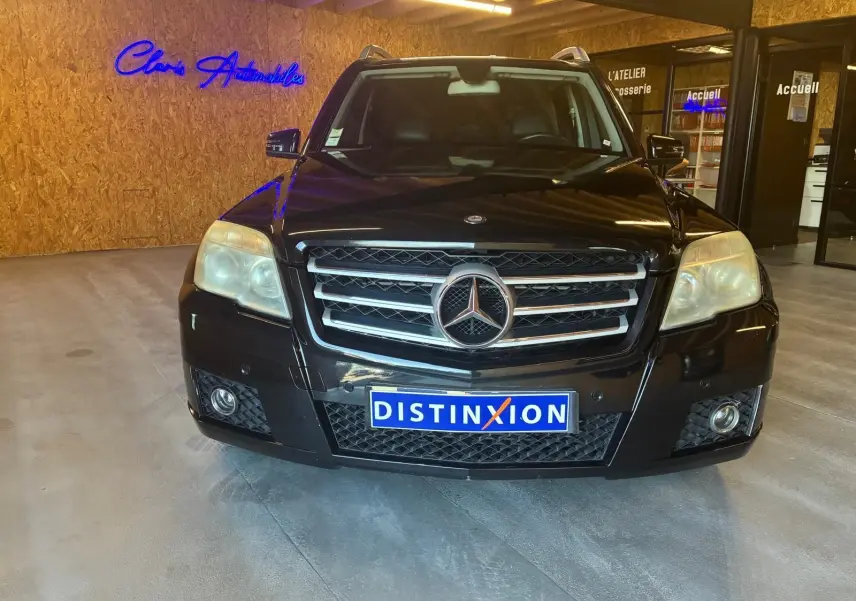 Vue de face d'un Mercedes GLK noir 2012 avec calandre chromée et plaque d'immatriculation DISTINXION en intérieur showroom.