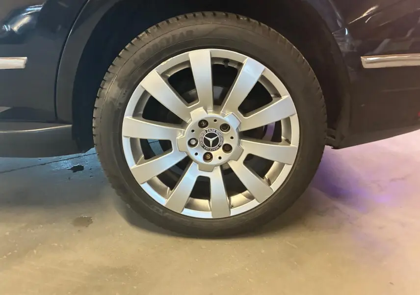 Gros plan sur la roue avant droite argentée d’un Mercedes GLK noir, mettant en valeur la jante étoile et le logo central.