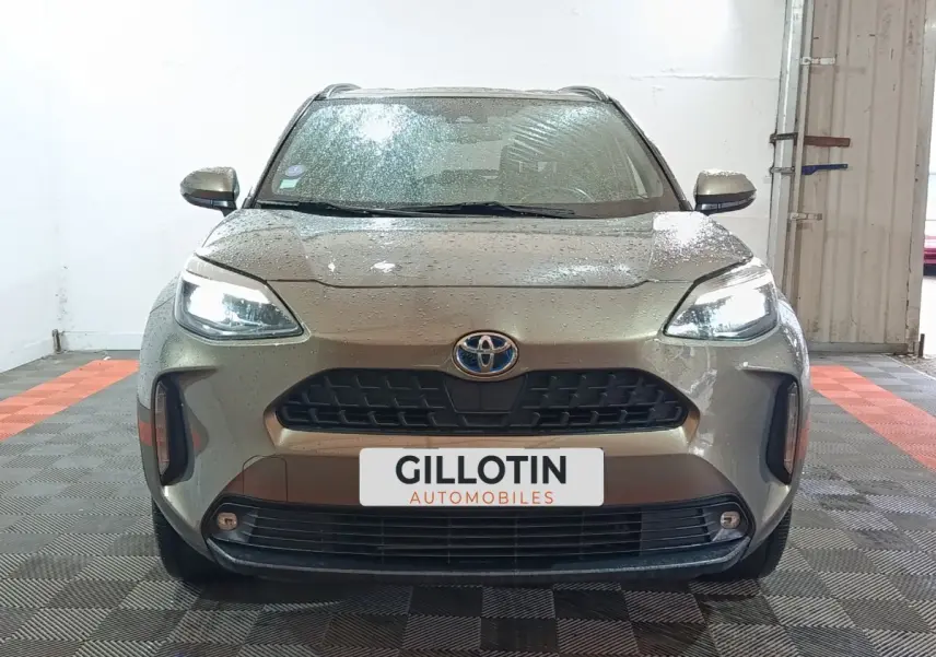 Vue frontale d'une Toyota Yaris Cross gris foncé avec phares LED allumés dans un garage.