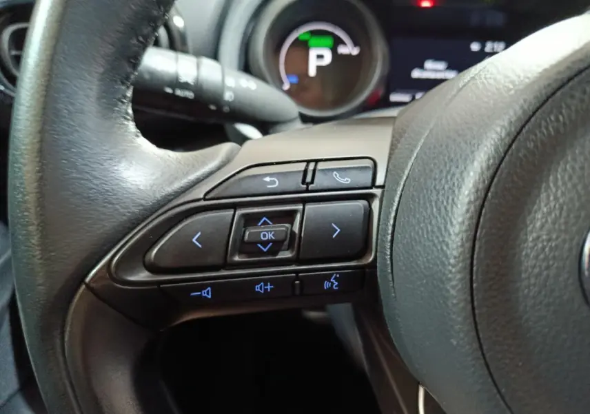 Gros plan sur les commandes au volant à gauche du Toyota Yaris Cross 1.5 Hybrid 116h Design Auto, tableau de bord en arrière-plan.