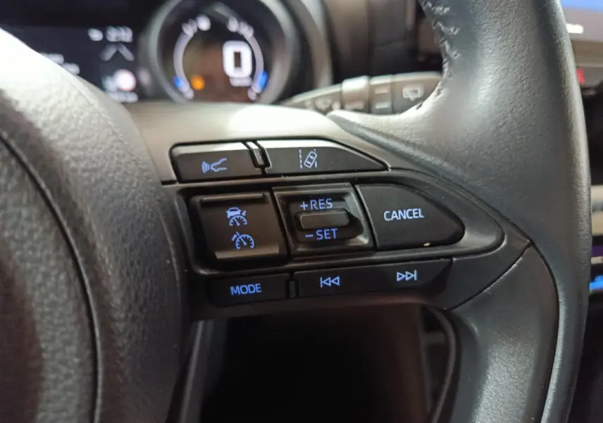 Gros plan sur les commandes du volant cuir noir du Toyota Yaris Cross 1.5 Hybrid 2022, avec régulateur adaptatif et fonctions vocales.