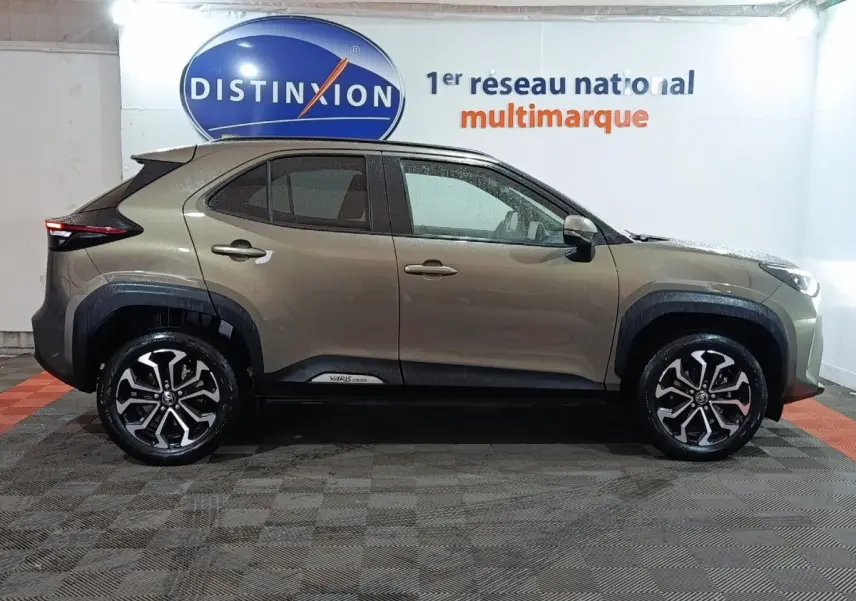 Toyota Yaris Cross gris foncé vue de profil côté gauche, avec jantes alliage et protections noires autour des roues.