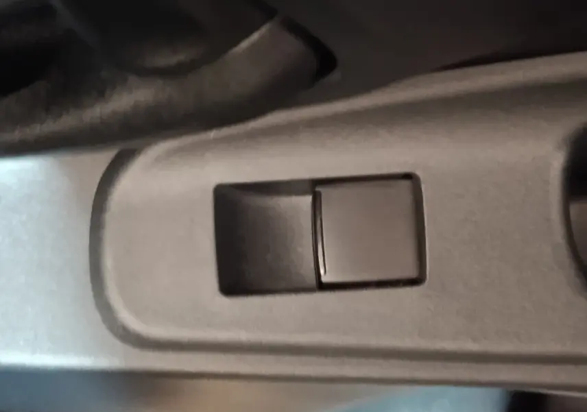 Gros plan sur le bouton de commande de la vitre côté conducteur dans l'habitacle gris foncé d'une Toyota Yaris Cross 2022.