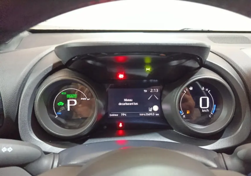 Vue rapprochée du combiné d'instruments digital de la Toyota Yaris Cross 1.5 Hybrid 116h, affichant un avertissement de niveau carburant bas.