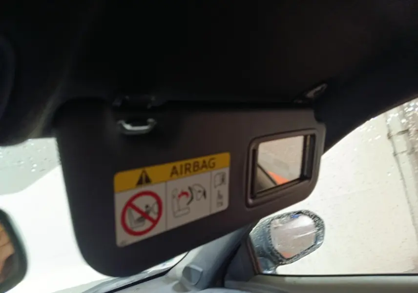 Détail intérieur du pare-soleil côté conducteur avec miroir et avertissement airbag, rétroviseur extérieur visible sous la pluie.