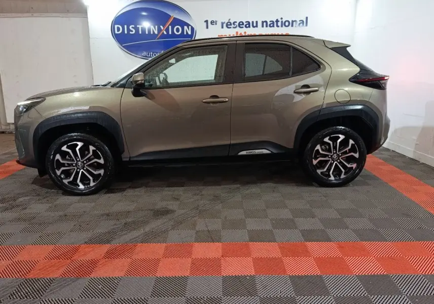Vue de profil côté gauche d'une Toyota Yaris Cross gris foncé avec jantes alliage et protections noires autour des passages de roues.