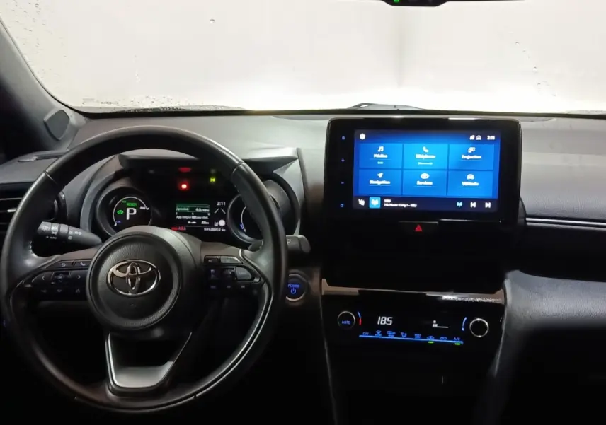 Vue intérieure frontale du tableau de bord et volant cuir noir du Toyota Yaris Cross hybride 2022 avec écran tactile central allumé.