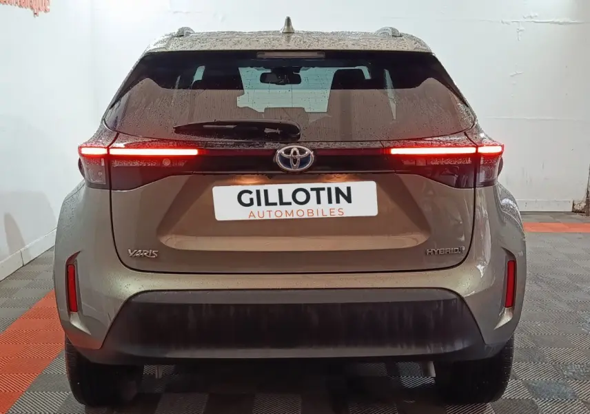 Vue arrière d'une Toyota Yaris Cross gris foncé avec feux arrière LED allumés dans un garage.