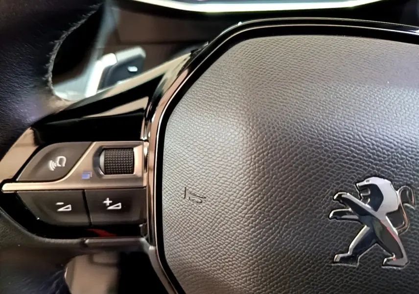Gros plan sur le volant cuir noir multifonctions du Peugeot 2008 blanc, avec logo lion chromé visible au centre.