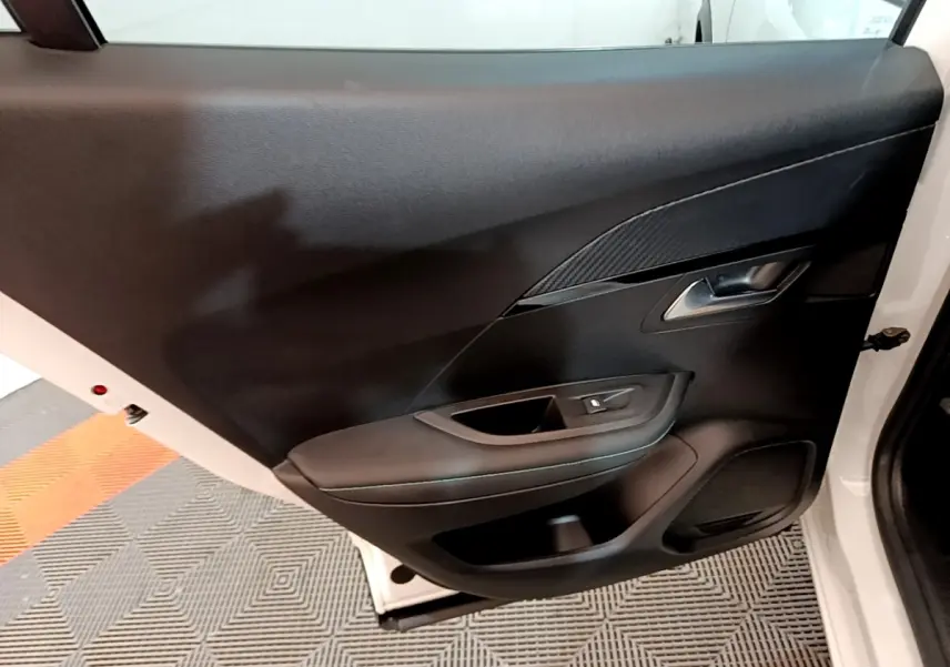 Vue intérieure de la porte arrière droite d'un Peugeot 2008 blanc, avec garniture noire et poignée argentée.