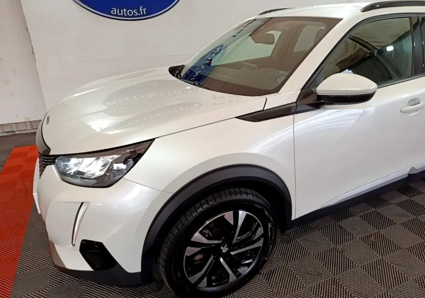 Vue 3/4 avant droit d'un Peugeot 2008 blanc avec jantes noires et détails noirs contrastants sur ailes et rétroviseur.