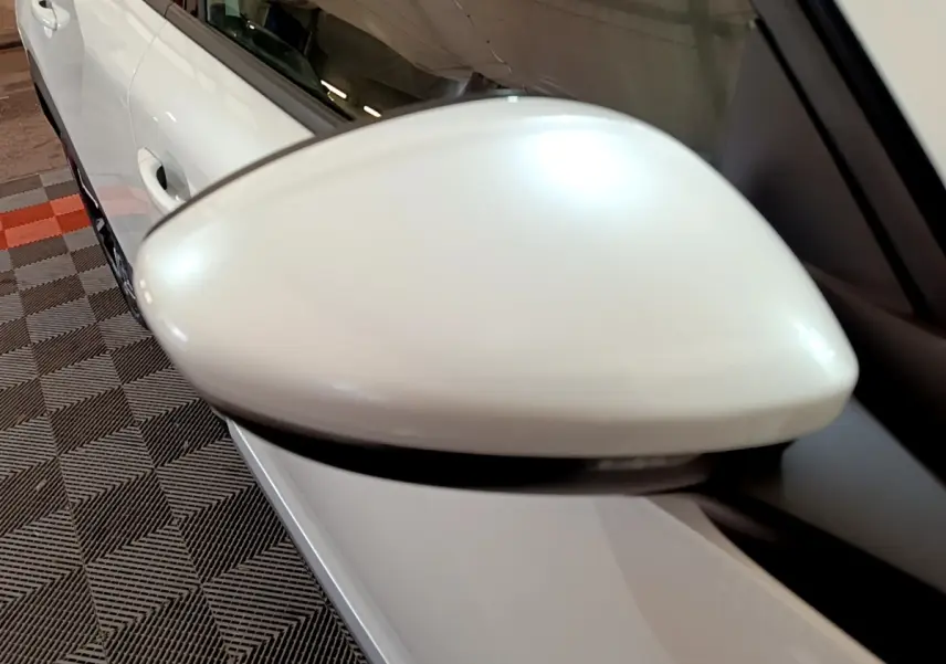 Gros plan sur le rétroviseur droit blanc d’un Peugeot 2008 blanc, avec une partie de la portière visible en arrière-plan.